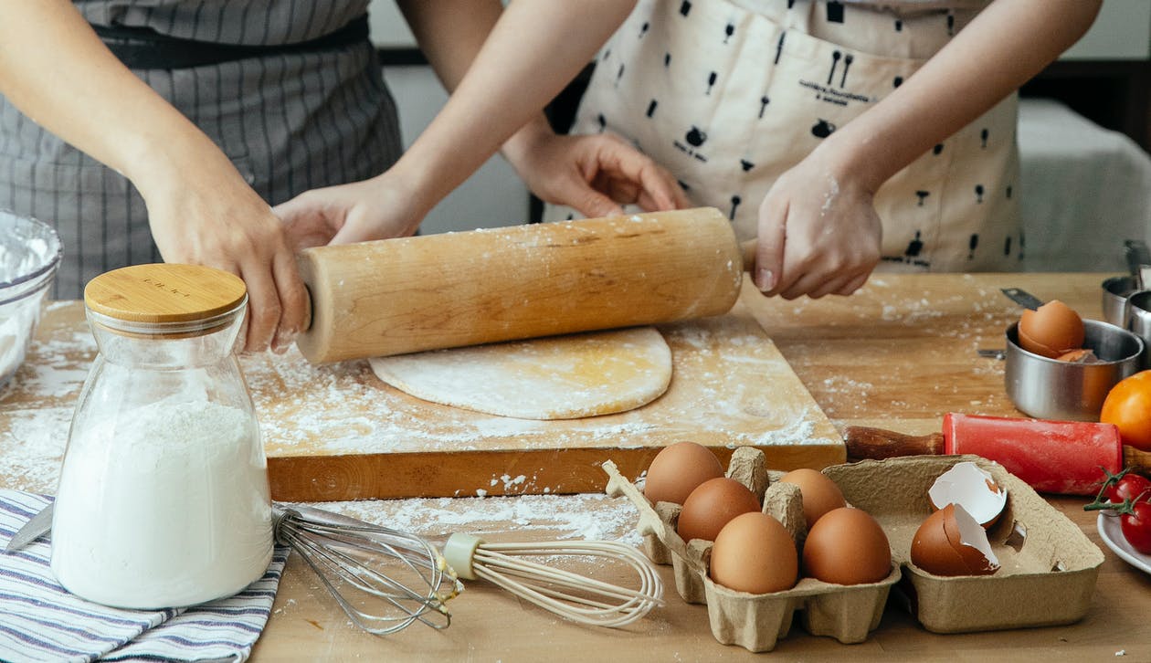 Free Unrecognizable women rolling dough together on board on table with jar with flour carton with eggs and whisks Stock Photo